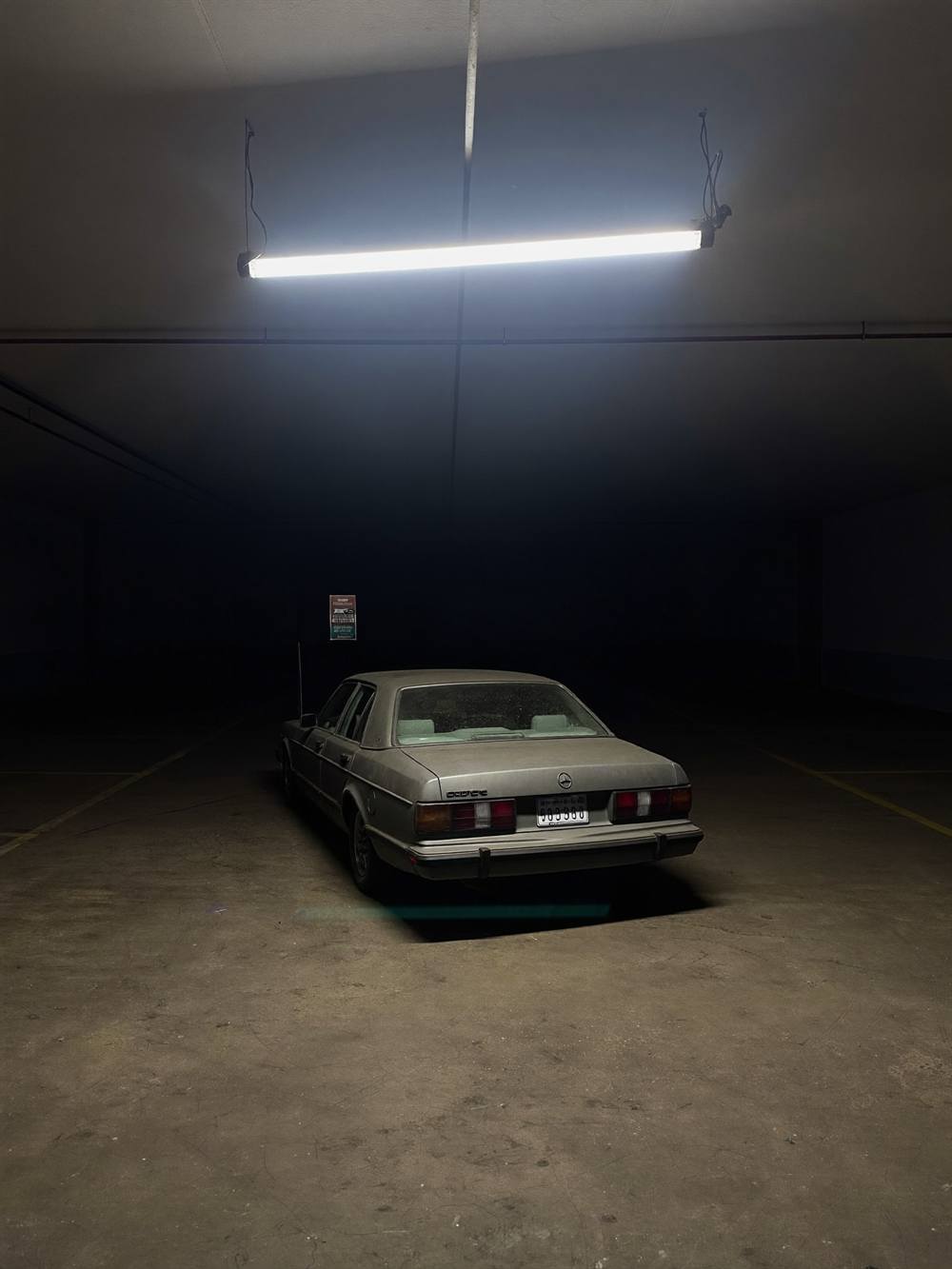 One old sedan alone under a single light in an empty garage