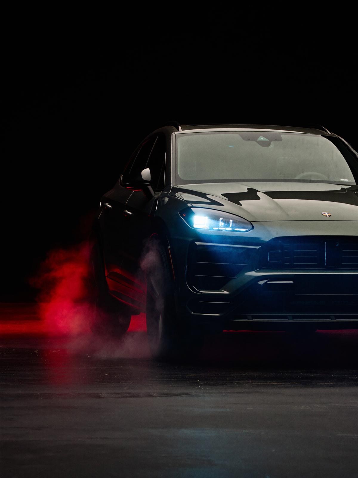 Performance SUV emerging from red smoke in a dark studio, headlights on
