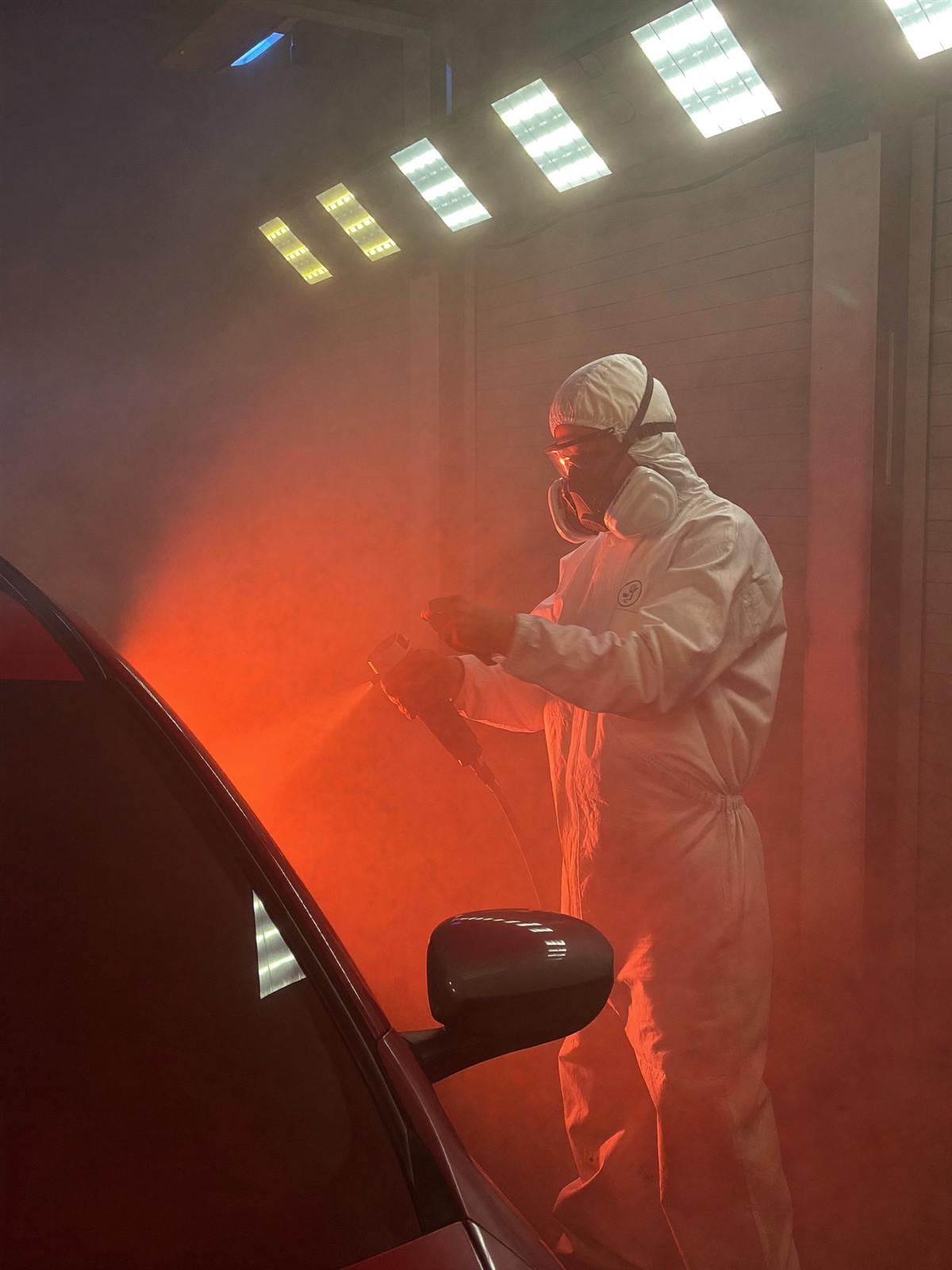 Painter in a white suit spraying red paint in a Dubai booth filled with red haze