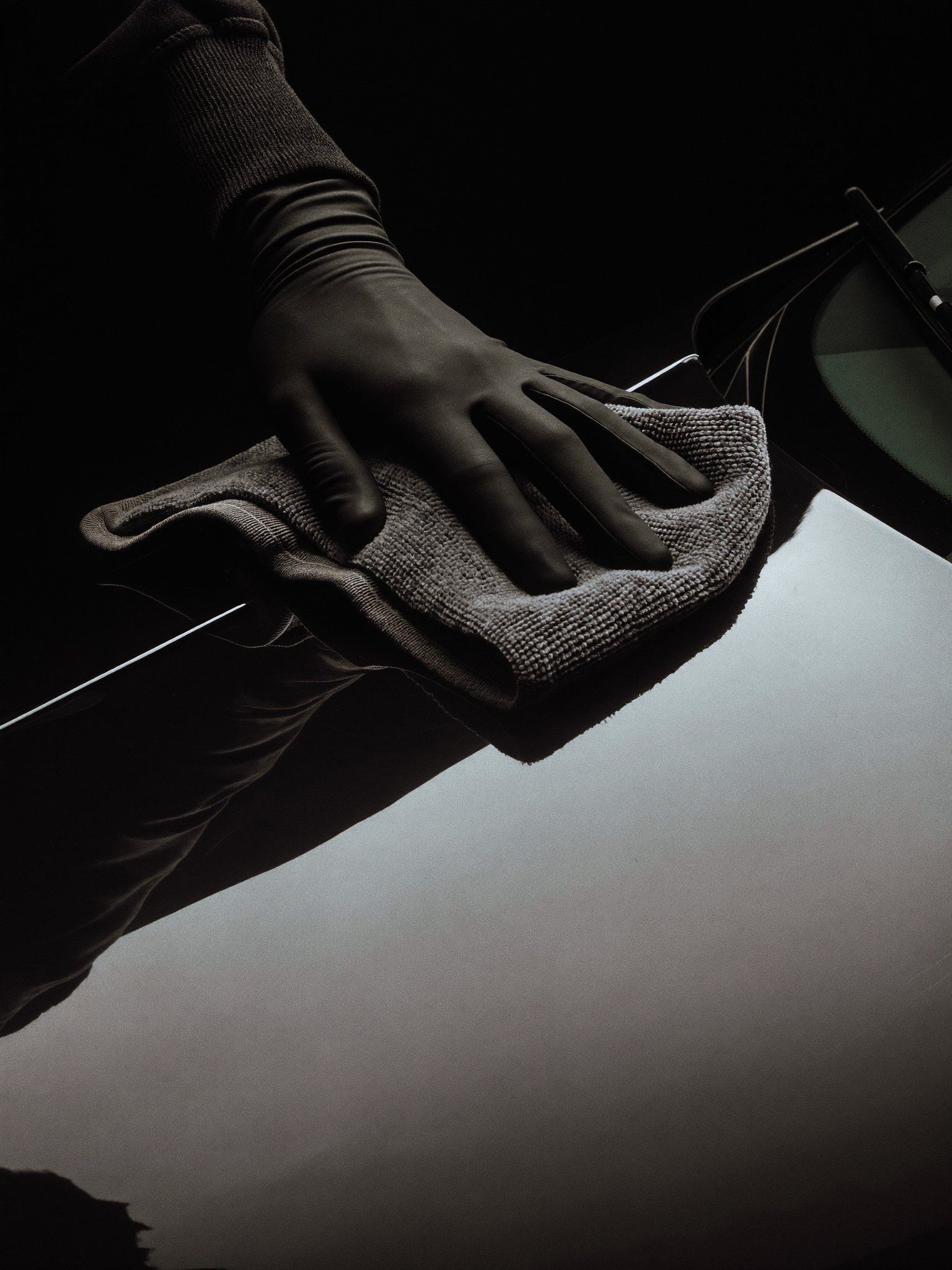 A gloved hand buffing a glossy black panel with a microfiber cloth